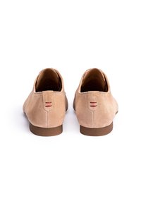 Chaussures en daim beige avec des talons bas, des arrière arrondis et des accents de couture rouge contrastants. Texture lisse et design simple.