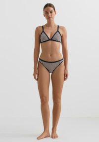 Csíkos bikini szett háromszög alakú bralettel, vékony pántokkal és hozzáillő, alacsony derekú alsóval, tengerészkék és krémszínben. Sima anyag textúra.