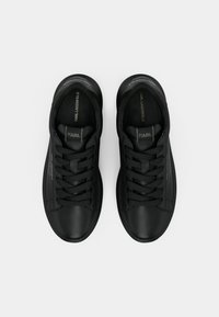Zapatillas negras de material suave con puntera redondeada, cordones prominentes y una marca en la lengüeta y los laterales.