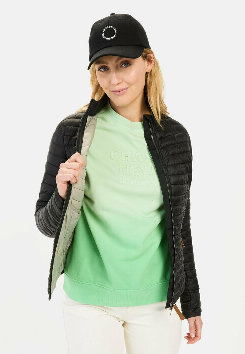 Black puffer jacket with textured fabric, light green sweatshirt underneath featuring embossed text, and a black cap with logo.