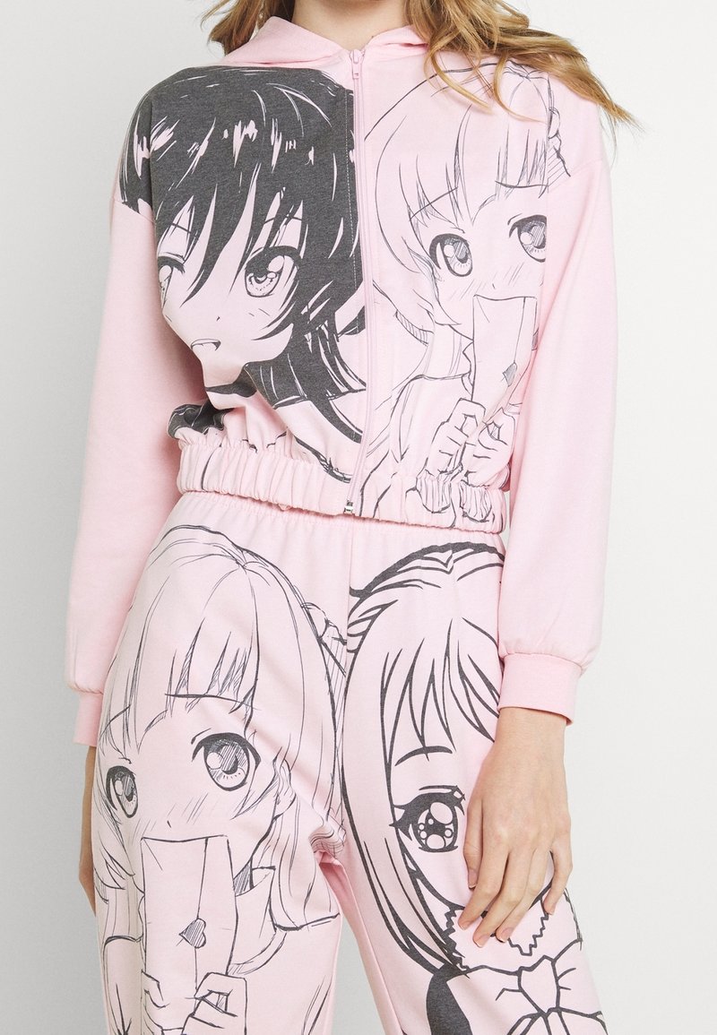 Completo con felpa e pantaloni rosa caratterizzato da illustrazioni grafiche nere di due personaggi. Il tessuto è morbido e presenta una vita e polsini elasticizzati.
