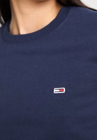 Sudadera de algodón azul marino con un pequeño logo bordado en rojo, blanco y azul en la parte izquierda del pecho. Diseño clásico de cuello redondo.