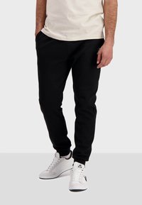 Svarta sweatpants med elastisk midja och mudd, gjorda av ett mjukt material. Matchat med vita sneakers med svarta detaljer.