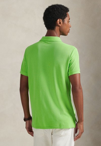 Grønn poloskjorte med korte ermer og krage, laget av teksturert stoff. Har sidesplitter, synlige sømmer og en løs passform.