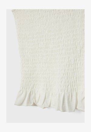 Valkoinen pusero, jossa on smokkikuvio. Varustettu röyhelöhelmalla. Valmistettu pehmeästä kankaasta, mikä korostaa kevyttä ja ilmavaa muotoilua.