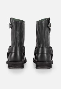 Botas de cuero negro hasta el tobillo con puntas redondeadas, hebillas laterales y correas texturizadas. Tacones bajos robustos y un acabado suave que realzan la durabilidad.