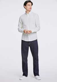 Ljusgrön linneknappskjorta, mörkblå jeans och vita sneakers; skjortan har lång ärm och en avslappnad krage; lös passform.