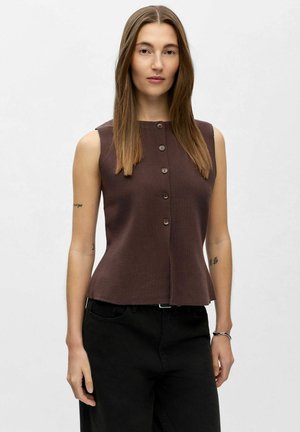 Top sans manches marron avec un col rond, présentant une fermeture à boutons sur le devant et un ourlet évasé. Porté avec un pantalon noir.