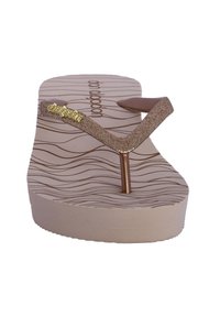Chancla con suela de goma beige, texturizada con patrones de olas. Las correas doradas brillantes tienen pequeños acentos decorativos en oro.