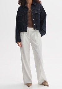 Mörk denimjacka med kort längd och två bröstfickor, i kombination med vita vida byxor och ljusbeige skor. Texturerad brun ribbad topp under.