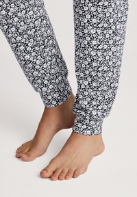 Zwart-witte broeken met een bloemenpatroon en een strakke manchette, weergegeven boven blote voeten op een effen achtergrond.