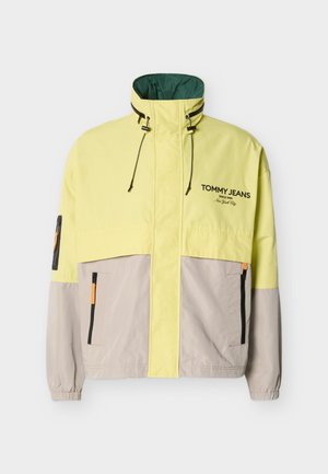 Halv-gul, halv-grå jakke med glidelås, høy krage, justerbare snorer, elastiske mansjetter, sidelommer og "Tommy Jeans"-logo på brystet.