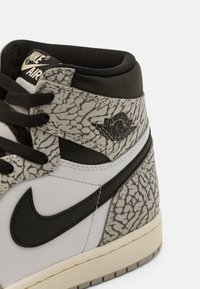 Gros plan d’une basket Air Jordan blanche et noire avec un imprimé éléphant gris texturé et un logo Nike swoosh noir.