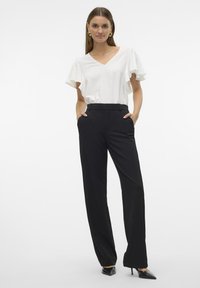 Bílý top s výstřihem do V a krátkými volánkovými rukávy v kombinaci s černými elegantními kalhotami. Slim fit a hladká textura, doplněné špičatými podpatky.