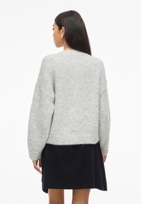 Pilkas megztinis su laisvu prisitaikymu, raukšlėtomis rankovėmis ir apatine dalimi. Minkšta tekstūra, su šiek tiek trumpa ilgio ir nuleistais pečių siūlais.