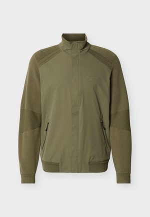 Veste zippée vert olive avec col montant, poignets et ourlet côtelés, manches en tricot texturé, et logo "Porsche BOSS" sur la poitrine.