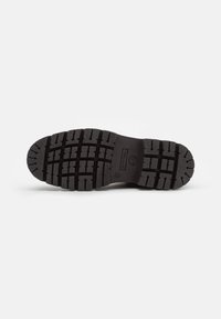 Suela de bota de goma negra con un patrón de tracción robusto, que presenta surcos profundos y un logo en relieve en el centro.