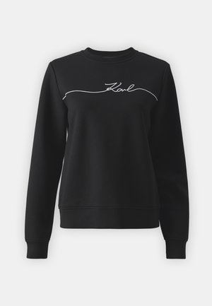 Sweatshirt negru din țesătură moale, cu guler rotund, mâneci lungi și text brodat alb "Karl" pe piept.