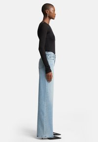 Lichtblauwe wijde jeans van denim, gecombineerd met een aansluitend zwart langmouwen shirt. De outfit heeft een gladde textuur en een hoge taille.