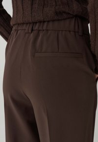 Bruine broek met een gladde stof, elastische tailleband en een enkele achterzak met een gestroomlijnd ontwerp.