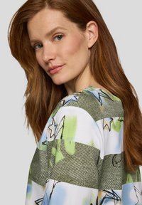 Gemusterte Bluse mit Streifen in Grün, Blau und Weiß, mit Sternmotiven und einer weichen Textur. Rundhalsausschnitt und lockere Passform.