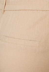 Tessuto di lino beige con una texture sottile; presenta una tasca a patch stretta cucita nella parte posteriore, con cuciture minime visibili.
