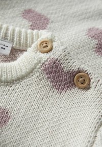 Sweter z dzianiny w odcieniu kremowym, zdobiony różowymi wzorami serc. Posiada ribbawany dekolt oraz dwa drewniane guziki przy kołnierzu. Miękka faktura.