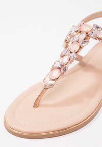 Rose gold thong sandal with embellished strap featuring pink and clear stones, soft beige footbed, and thin metallic detail on sole.
