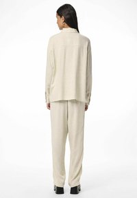 Set di camicia e pantaloni in lino beige chiaro con una vestibilità libera, caratterizzato da un colletto e maniche lunghe. I pantaloni hanno un taglio dritto. Semplice e testurizzato.