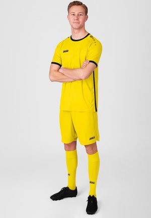 Gelbes Fußballtrikot mit kurzärmeligem Shirt, passenden Shorts und Socken. Schwarze Akzente am Kragen und Logo. Texturiertes Material und sportlicher Schnitt.