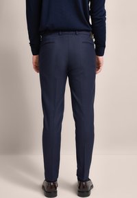 Navy dress pants with a slim fit, flat front, and back pockets. Made from smooth fabric, featuring a subtle sheen and tailored design.