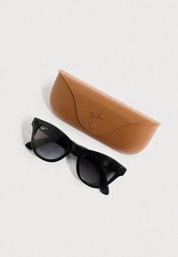 Occhiali da sole neri con montatura a forma di occhio di gatto, con lenti a sfumatura graduale, accanto a una custodia in pelle marrone con una texture liscia e logo.