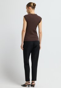 Brązowy prążkowany top bez rękawów z falbaną przy dekolcie, w połączeniu z czarnymi spodniami i czarnymi sandałami na obcasie, widok z tyłu.