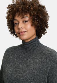 Grauer Strickpullover mit einem gerippten hohen Kragen, weicher Textur und lockerer Passform. Subtile Farbvariationen im Stoff.