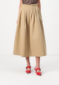 Kaki midi szoknya redőzésekkel, könnyű anyagból készült. Piros lakk slingback sarkú cipővel párosítva, hegyes orral és fémes díszítésekkel.