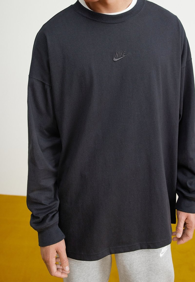 Svart långärmad t-shirt med rund halsringning och Nike-logotyp i mitten. Tillverkad av mjukt bomullstyg, har en avslappnad passform och ribbade ärmslut.
