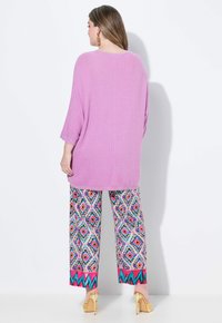 Rosa Strickpullover mit Dreiviertelärmeln, kombiniert mit bunten, geometrisch gemusterten weiten Hosen, die pinke und teal Akzente aufweisen.