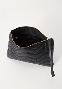 Černá prošívaná kožená kabelka na ruku se zlatým zipem, s rukojetí a podšívkou uvnitř, která obsahuje malou kapsu na zip.