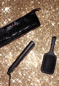 Schwarze hitzebeständige Tasche mit strukturiertem Design, ein eleganter schwarzer Haarglätter und eine passende Paddle-Bürste auf einem funkelnden goldenen Hintergrund.