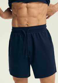 Chabrowe szorty bawełniane z elastycznym paskiem w talii i sznurkiem do regulacji. Posiada boczne kieszenie, luźny krój, gładką teksturę oraz swobodny styl.