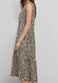 Vestido sin mangas con estampado floral en negro y crema, que presenta un diseño fluido con un dobladillo fruncido para aportar movimiento y textura.