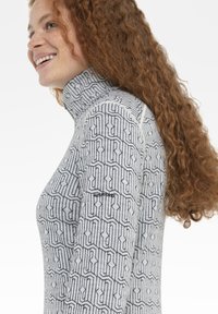 Grau hochgeschlossenes Oberteil mit einem gemusterten Design, das schwarze geometrische Linien zeigt. Weicher Stoff mit Logodetail auf dem Ärmel.