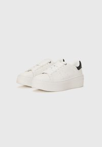 Vita plattformssneakers i slät syntetisk materia, med en svart klackaccent, fyra öglor och diskret perforerad detalj på sidorna.