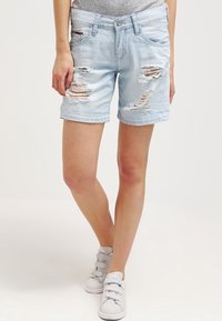 Ljust blå denimshorts med slitningar, mitt på låret längd, femficksdesign och uppvikta benslut. Bärs med grå sneakers.