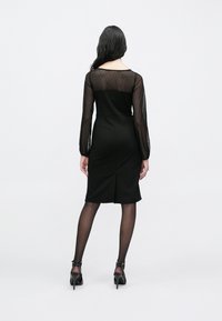 Must kleit, millel on liibuv siluett, läbipaistvad pikad varrukad täpilise tekstuuriga ja põlveni ulatuv lõige tagaosal lõhikuga.