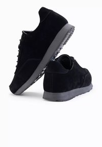 Mustat mokkasneakersit, joissa on pehmustettu harmaa pohja, pyöreä kärki ja nauhakiinnitys. Ominaisuuksiin kuuluu teksturoitu yläosa ja minimalistiset aksentit.