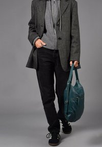 Abrigo de corte ajustado en gris oscuro sobre un suéter gris, combinado con pantalones negros y zapatillas. Se sostiene un bolso de cuero en color teal con un bolsillo con cremallera.
