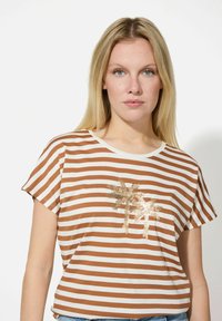 Gestreiftes T-Shirt in Braun und Creme mit kurzen Ärmeln, das ein goldenen Pailletten-Palmbaumdesign auf der Vorderseite zeigt. Weicher Stoff und lockere Passform.