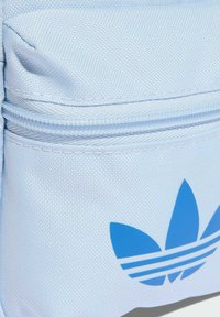 Bustina in tessuto azzurro chiaro con chiusura a zip, caratterizzata da un evidente logo adidas blu. Superficie testurizzata, design compatto con una piccola tasca.