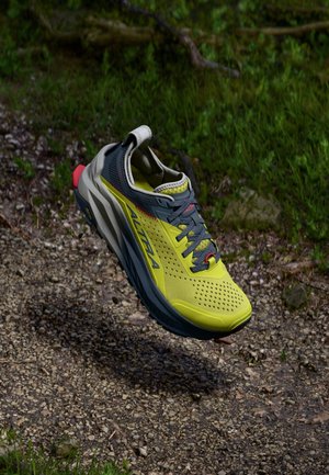 Chaussure de trail running avec un dessus en maille jaune, des accents gris, un talon rouge et une semelle texturée. Comprend des perforations pour la respirabilité et des détails réfléchissants.